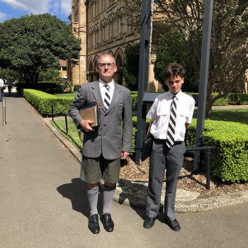 Mr Wayne Cox in uniform with a student by the school bell